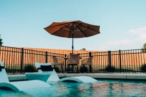 Backyard pool with in-water loungers, umbrella shade, and privacy fencing.