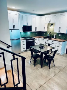 Finished basement kitchenette with white cabinetry, butcher block countertops, and modern black hardware.