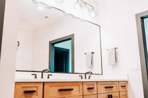 Double-sink bathroom vanity with light wood cabinetry, black fixtures, and framed mirrors.