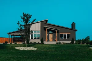 Front elevation of a modern custom home with covered entry, stone landscaping, and large windows.