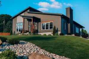 Side exterior view showing modern architecture, sloped lot, and decorative rock landscaping.