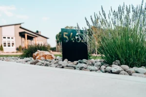 Landscaped driveway entrance with ornamental grasses, river rock, and custom address marker.