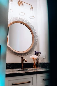 Powder room vanity with round decorative mirror, dark countertop, and modern fixtures.