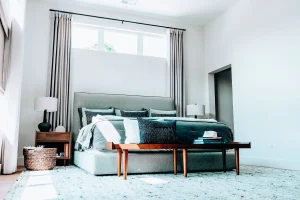 Primary bedroom with upholstered bed, large windows, and soft neutral finishes.